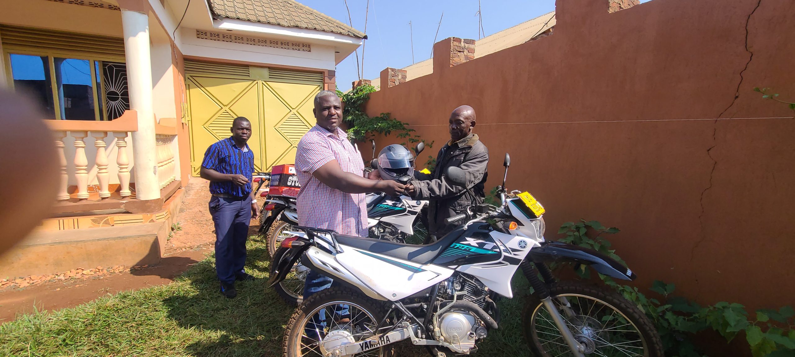 Agriculture Extension Officer Matayo Musigire receiving the Motorcycle from Walya Peter